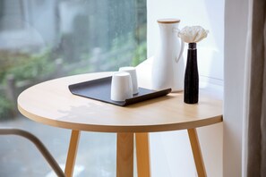 A round wooden table with a white pitcher, a black vase with a white flower, and two white cups on a black tray.