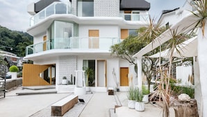 A modern multi-story house with a white exterior, a balcony, and a garden area with potted plants and a wooden bench. - Floral Hotel Hangzhou Lvpin Designer (Hangzhou)