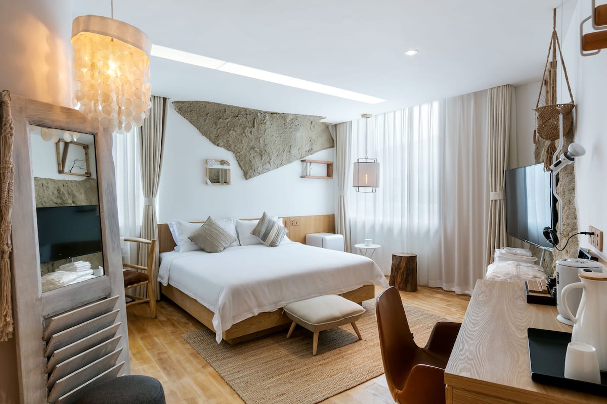 Une chambre d’hôtel moderne dotée d’un grand lit, d’un bureau avec une machine à café, d’une télévision et d’un mur en pierre original qui constitue un élément décoratif unique.