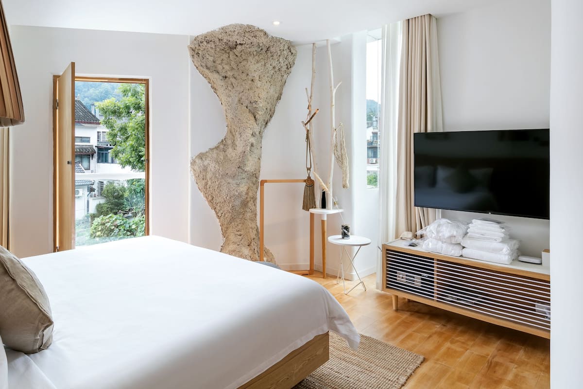 Une chambre d’hôtel moderne dotée d’un grand lit, d’un téléviseur à écran plat, d’un élément décoratif original rappelant une paroi rocheuse, et offrant une vue sur la ville par la fenêtre.