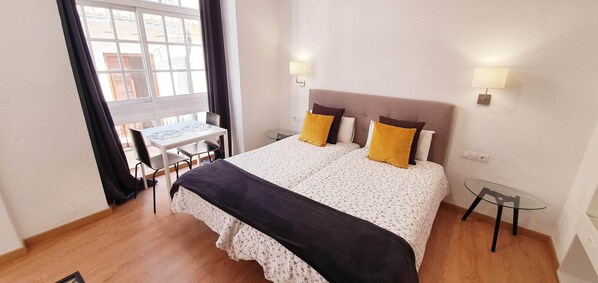 A bedroom with a bed, bedside lamps, a small table, and a window with curtains.