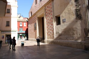 A courtyard with a tiled floor, a building with a patterned facade, and a sign for 'Herboristeria'.