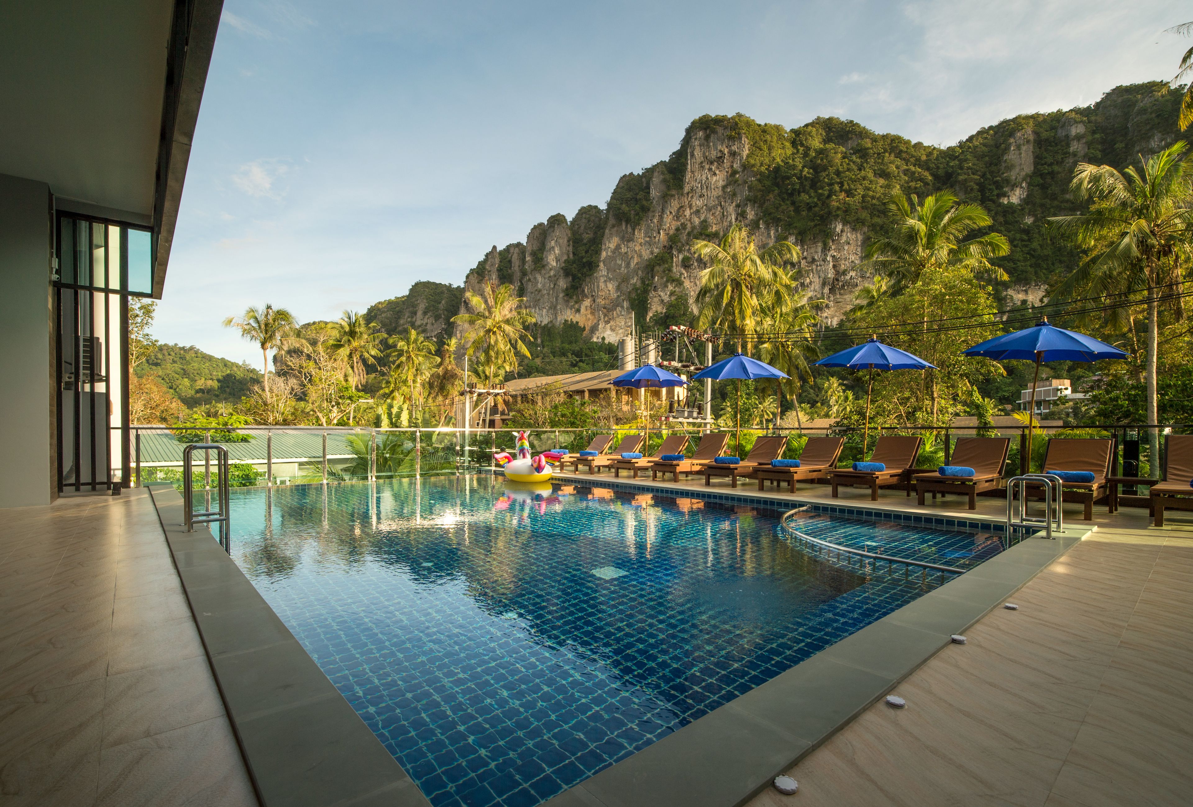 Une piscine entourée de chaises longues et de parasols, bordée de palmiers et avec une chaîne de montagnes en toile de fond.