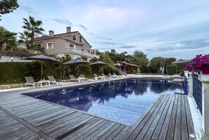 A swimming pool with lounge chairs and umbrellas, surrounded by a wooden deck and a large house with a balcony. - Terre de Rêve (Le Rouret)