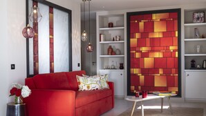 Una sala de estar moderna con un sofá rojo, cojines decorativos, un jarrón con flores, una mesa de centro y una estantería con diversos objetos.