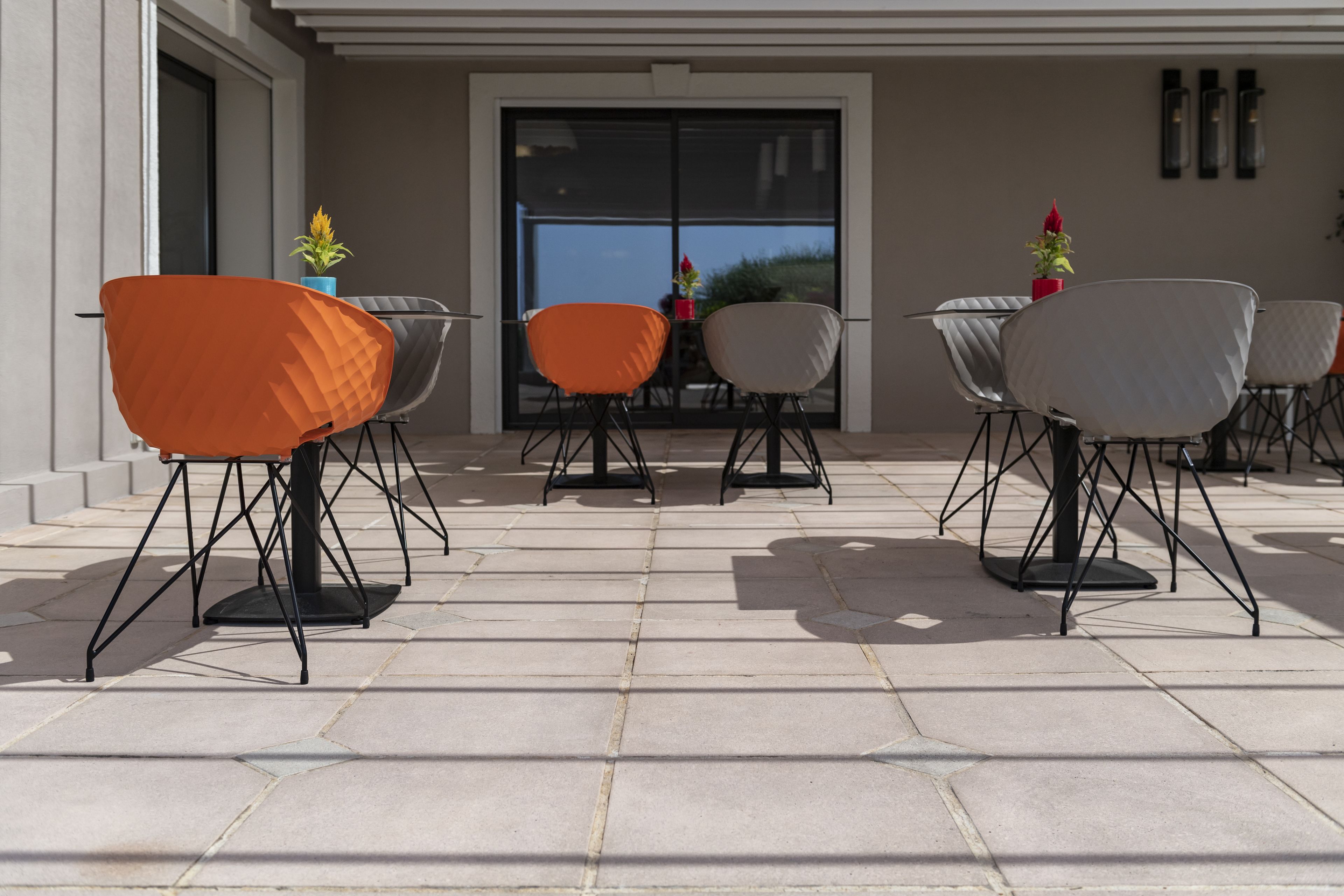 An outdoor patio with hexagonal tiles, modern chairs with metal legs, and potted plants.