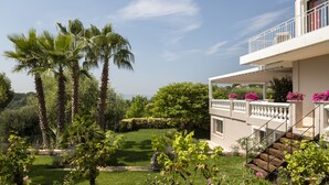 Una casa moderna con balcón, un jardín cuidado con palmeras y un cielo despejado.