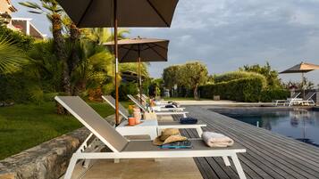A poolside area with lounge chairs, umbrellas, and a swimming pool.