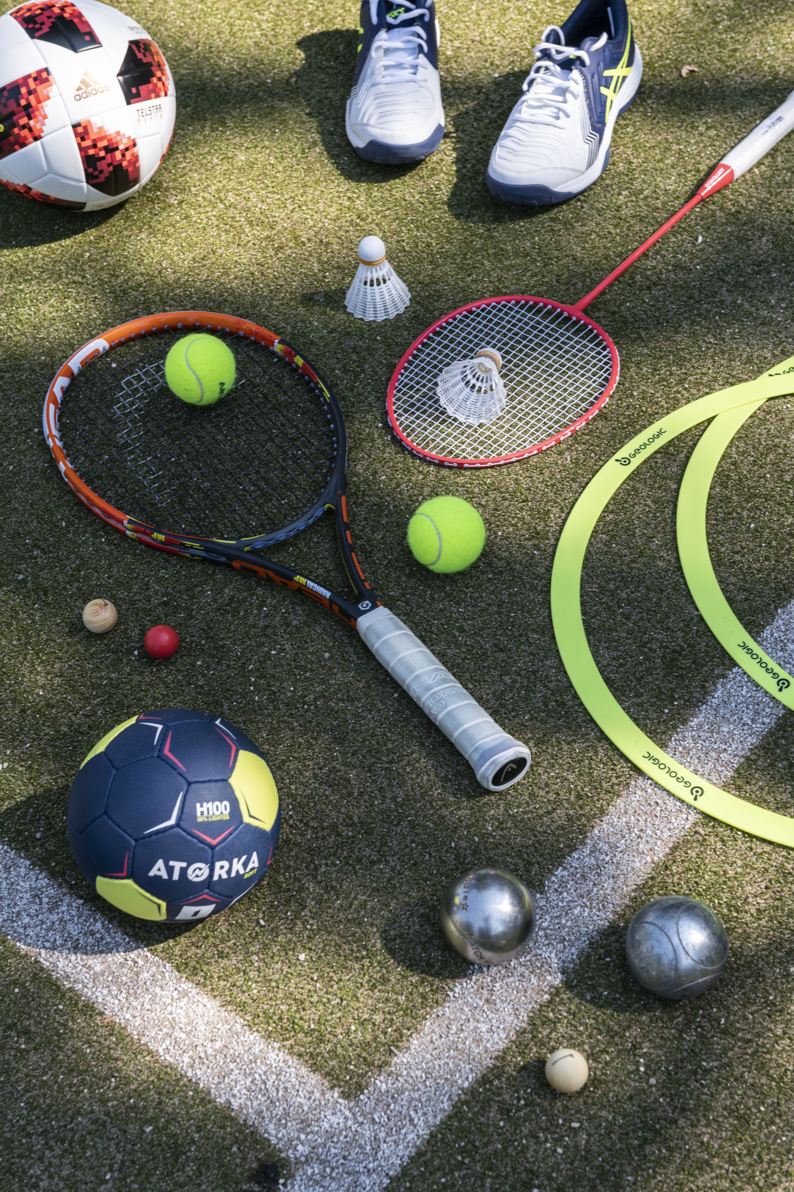 A variety of sports equipment, including tennis rackets, a shuttlecock, and multiple balls, arranged on a textured surface.