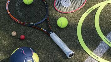 A variety of sports equipment, including tennis rackets, a shuttlecock, and multiple balls, arranged on a textured surface.