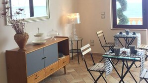 A dining area with a glass table and chairs, a wooden cabinet with drawers, and a lamp.
