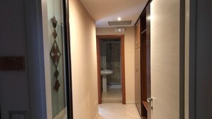 A narrow hallway with a glass door on the left, a wooden door on the right, and a bathroom visible in the background.