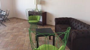 A living room with a green chair, a brown sofa, a painting of the ocean on the wall, and a lamp on a table.