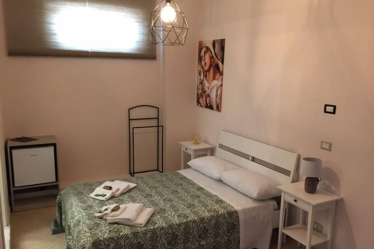 Habitació d'hotel amb un llit, taules de nit, una làmpada, un quadre i una finestra.