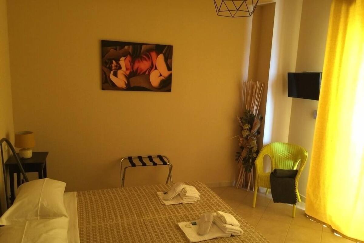 Habitació d'hotel amb un llit, una cadira, un quadre i una televisió penjada a la paret.