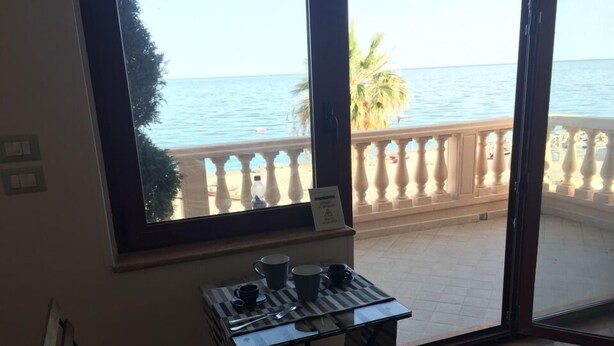 A balcony with a view of the sea, a table with cups and a sign, and a bench.