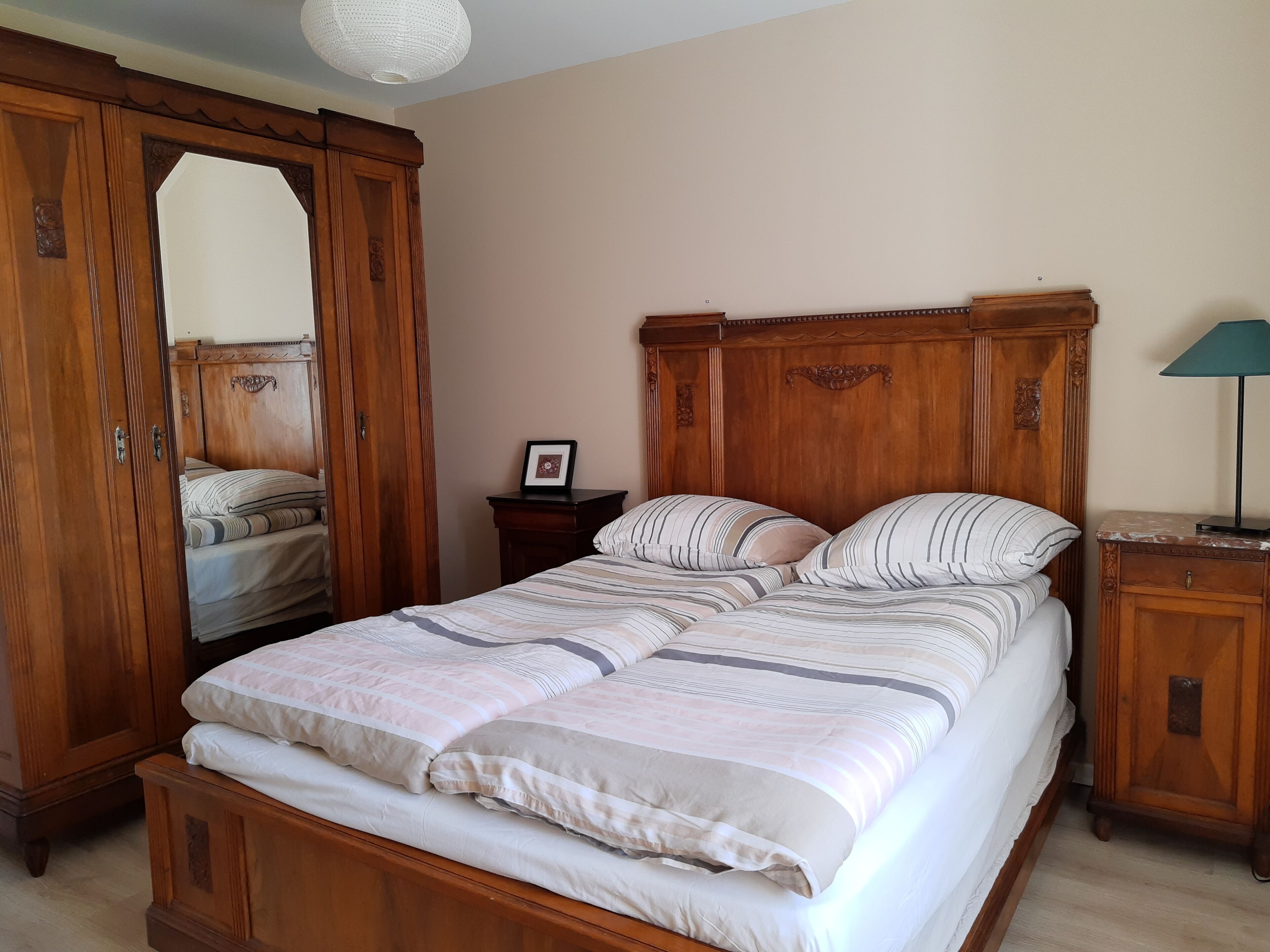A bedroom with a wooden bed, a nightstand, a dresser, and a mirror.