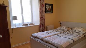 Ein Schlafzimmer mit Bett, einem Fenster mit Vorhängen, einem Heizkörper und einem Bild an der Wand.