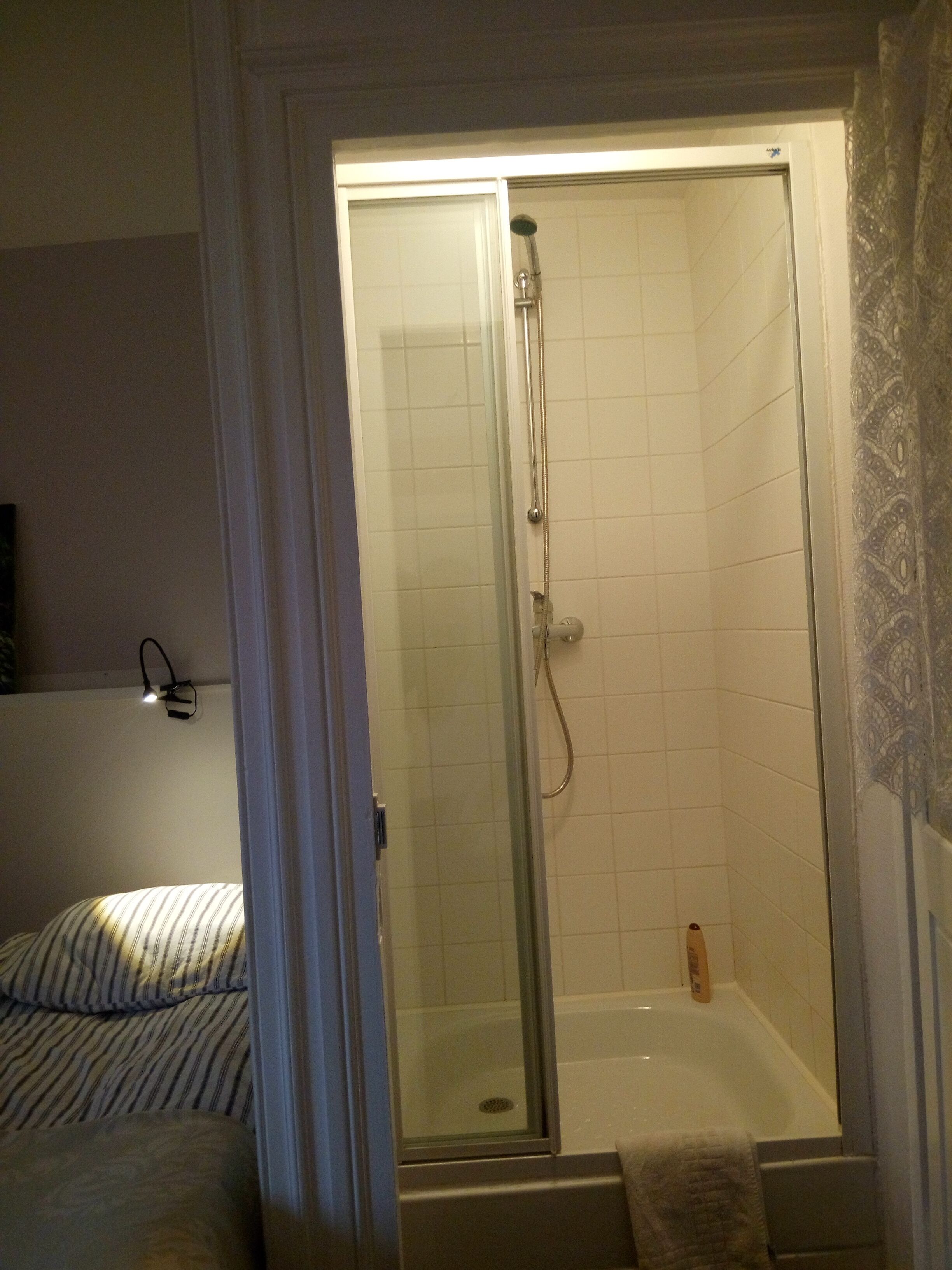 Un baño con ducha de vidrio, bañera y cama con ropa de cama a rayas.