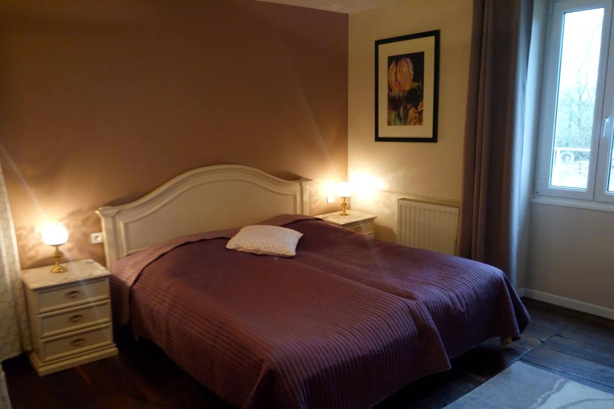 Ein ordentlich bezogenes Bett mit Kopfteil, ein Nachttisch mit Lampe und ein gerahmtes Bild an der Wand.