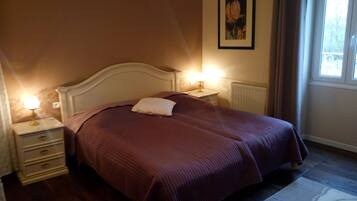 Un lit bien fait, avec une tête de lit, une table de chevet sur laquelle se trouve une lampe, et un tableau encadré accroché au mur.