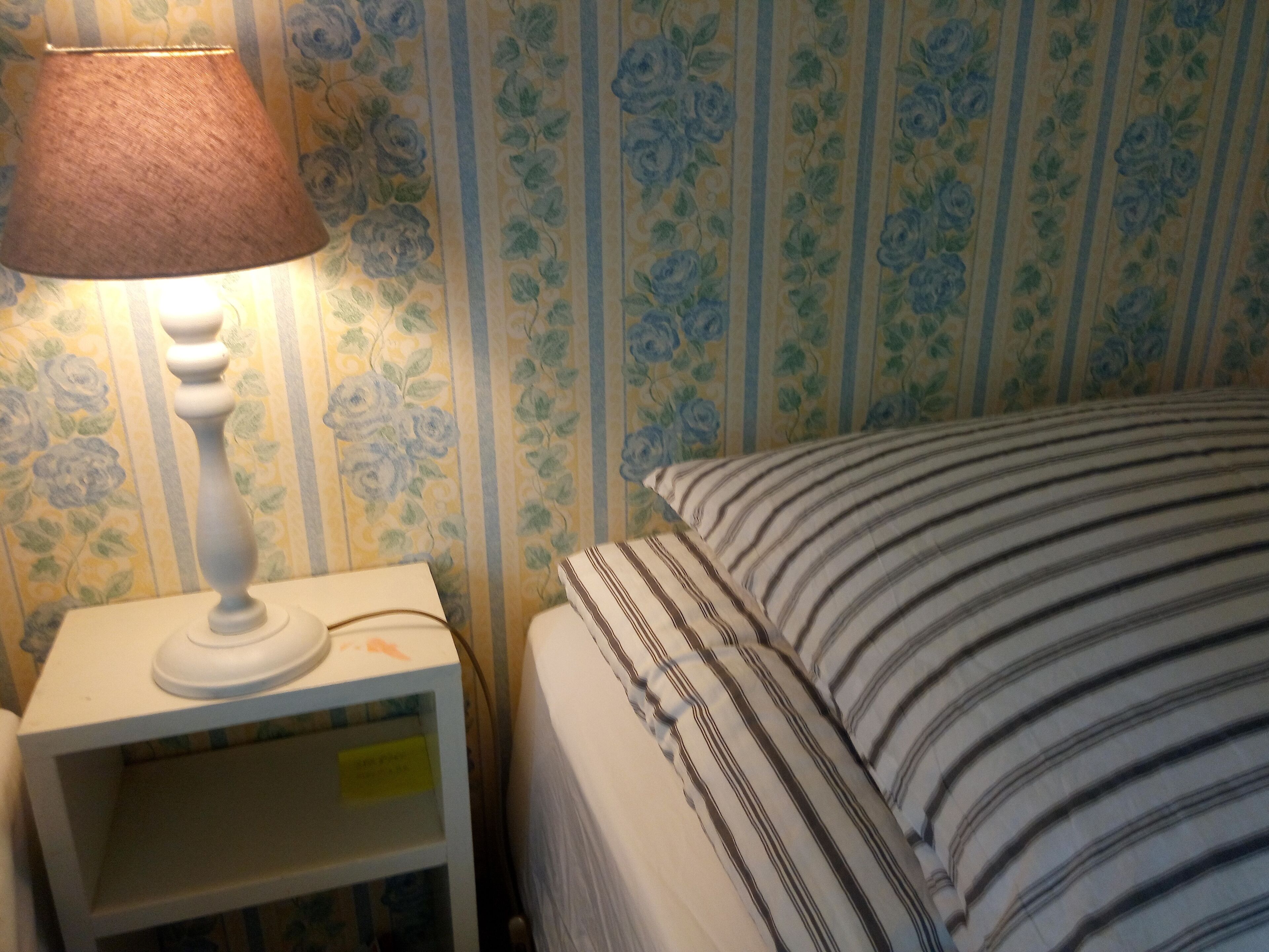 Un lit avec une literie à rayures, une table de chevet avec une lampe et un papier peint à motifs floraux.