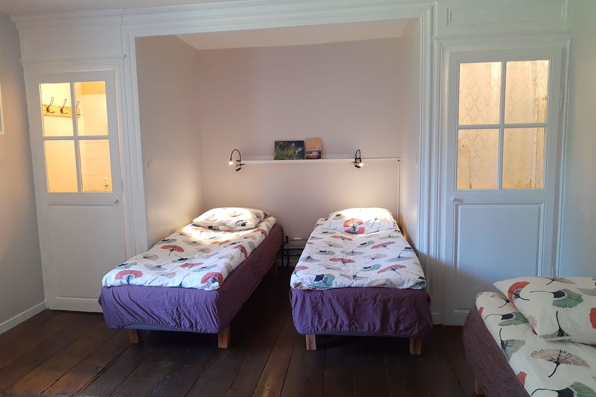 Ein kleines, gemütliches Zimmer mit zwei Einzelbetten, Holzboden und einer weißen Tür mit Glasfeldern.
