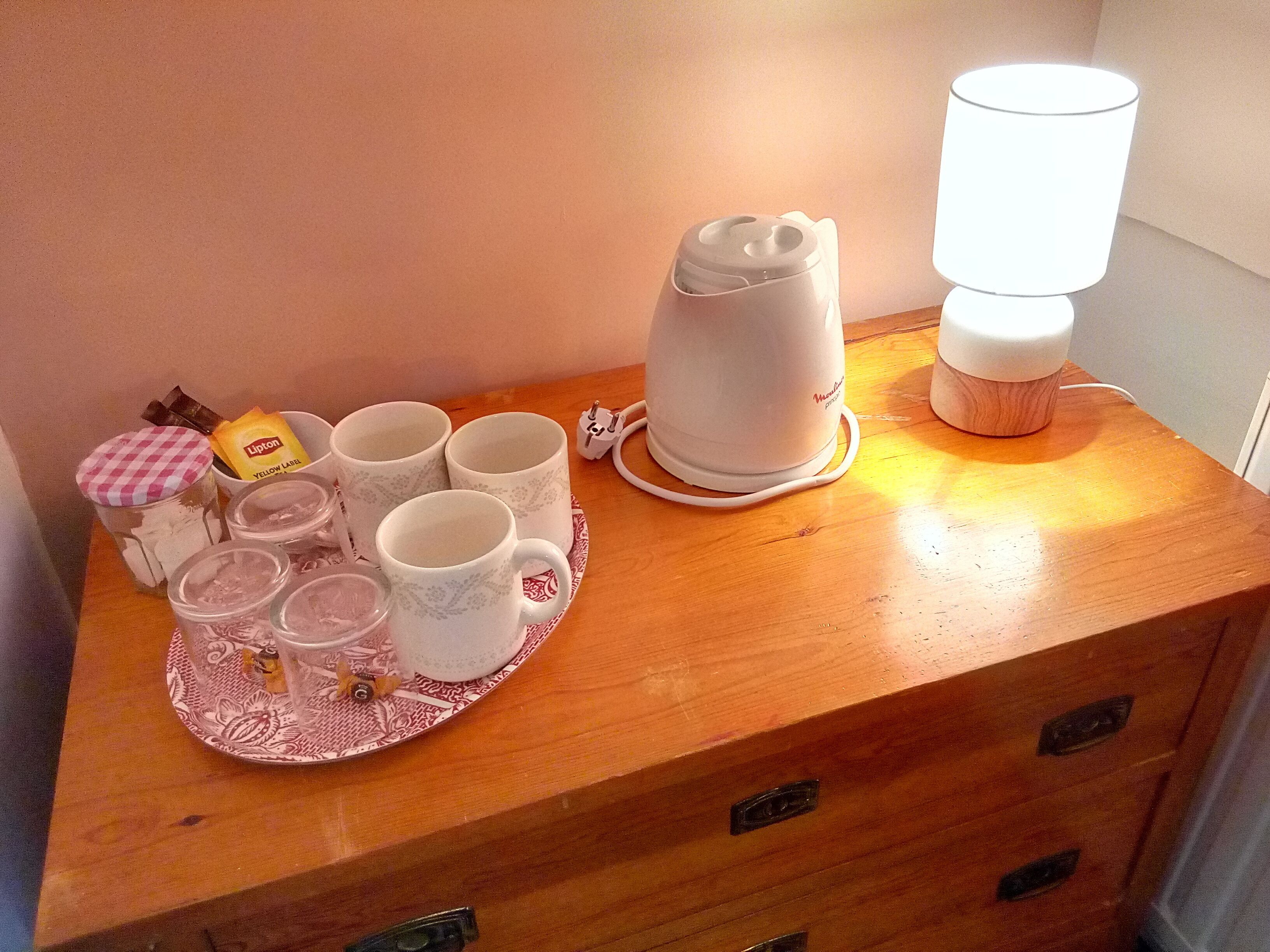 A wooden table with a tea set, including cups and a teapot, and a lamp.