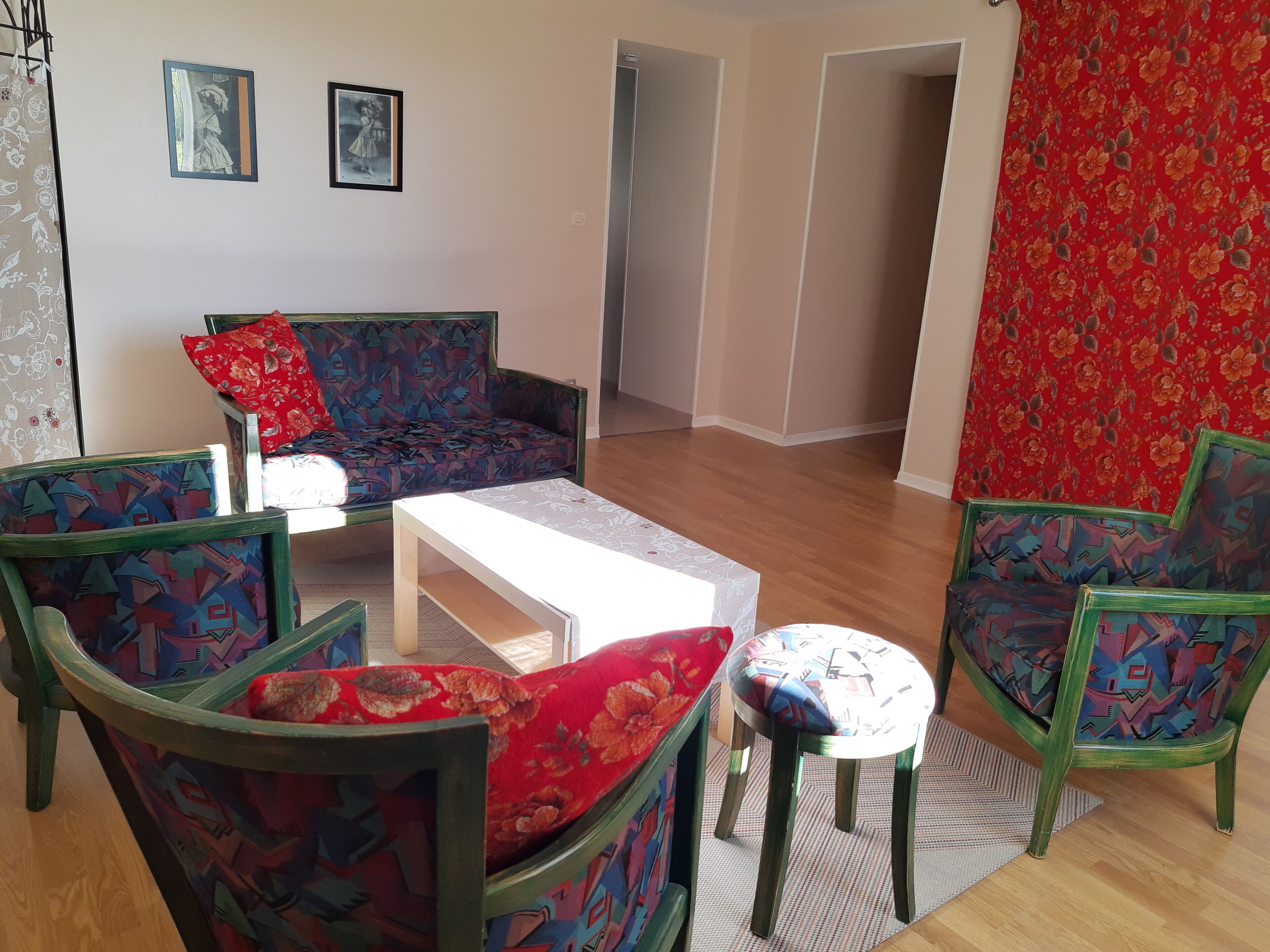 A living room with a sofa, two armchairs, a coffee table, and a rug. There are two framed pictures on the wall.