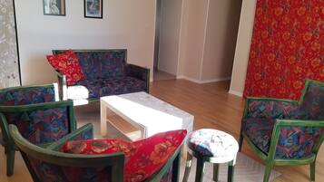 A living room with a sofa, two armchairs, a coffee table, and a rug. There are two framed pictures on the wall.