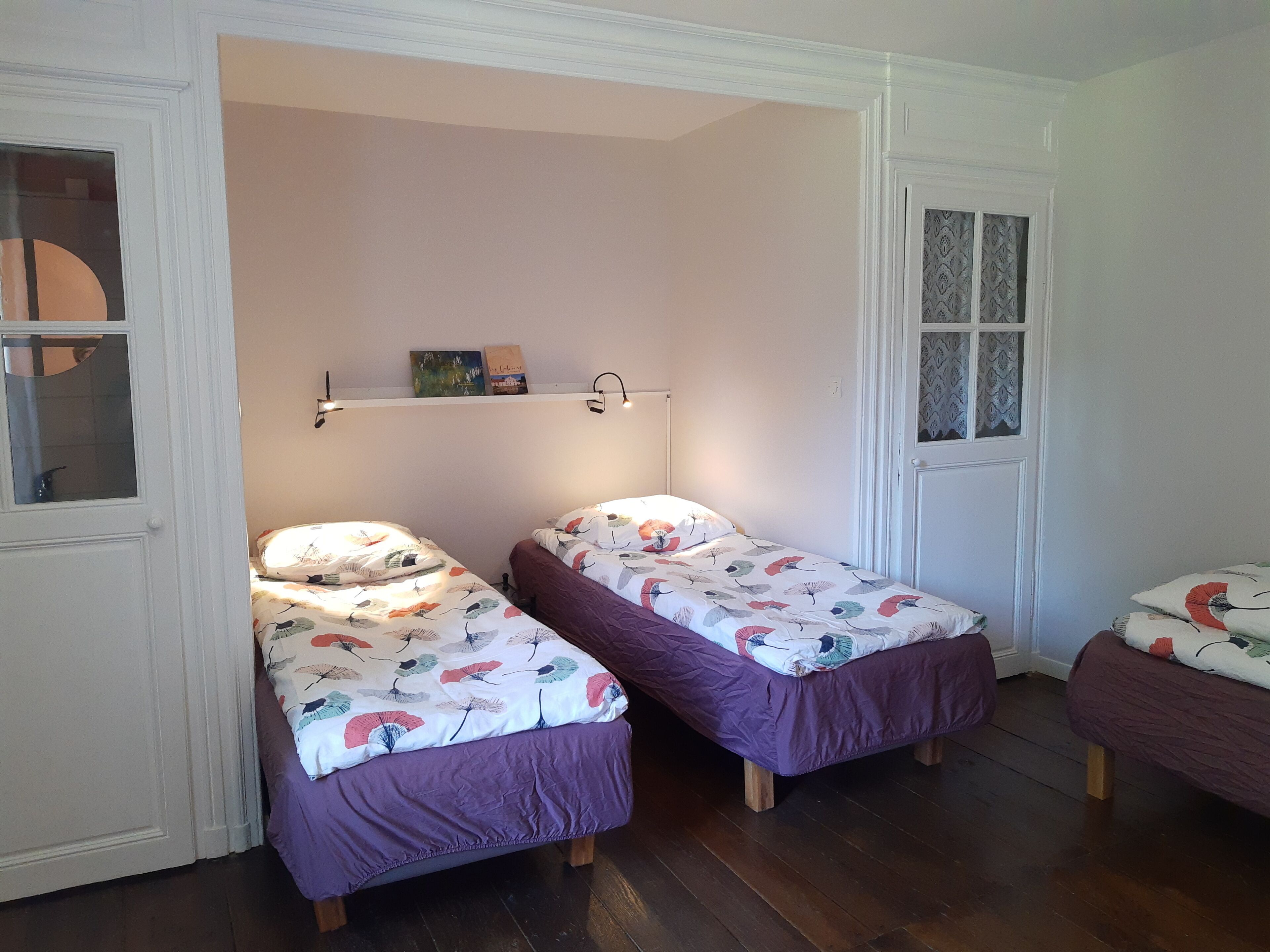 Una habitación con dos camas individuales, una ventana con cortinas estampadas y una estantería con libros y una pequeña planta.