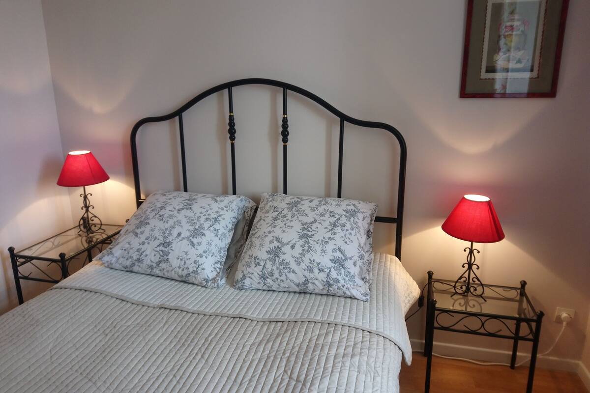 Ein Bett mit weiß gestopfter Bettdecke, zwei passende Kissen und zwei Nachttische mit roten Lampenschirmen.