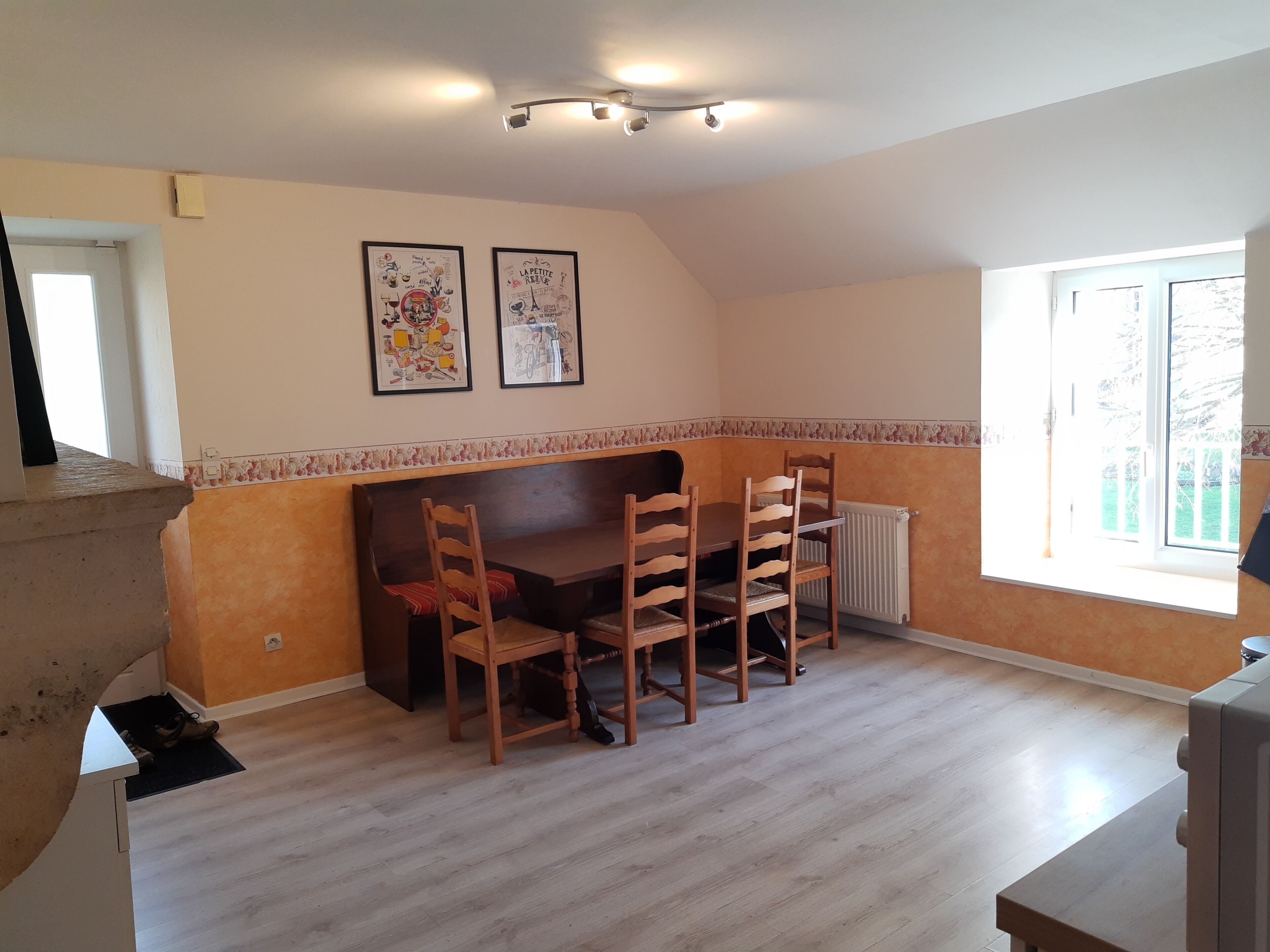 A dining area with a wooden table and chairs, a bench, and two framed pictures on the wall.