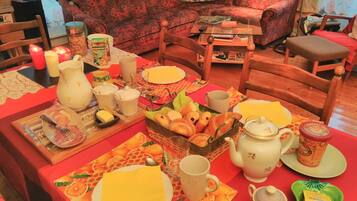 Una mesa de comedor dispuesta con platos, cubiertos y diversos alimentos, rodeada de sillas de madera y un sofá al fondo.
