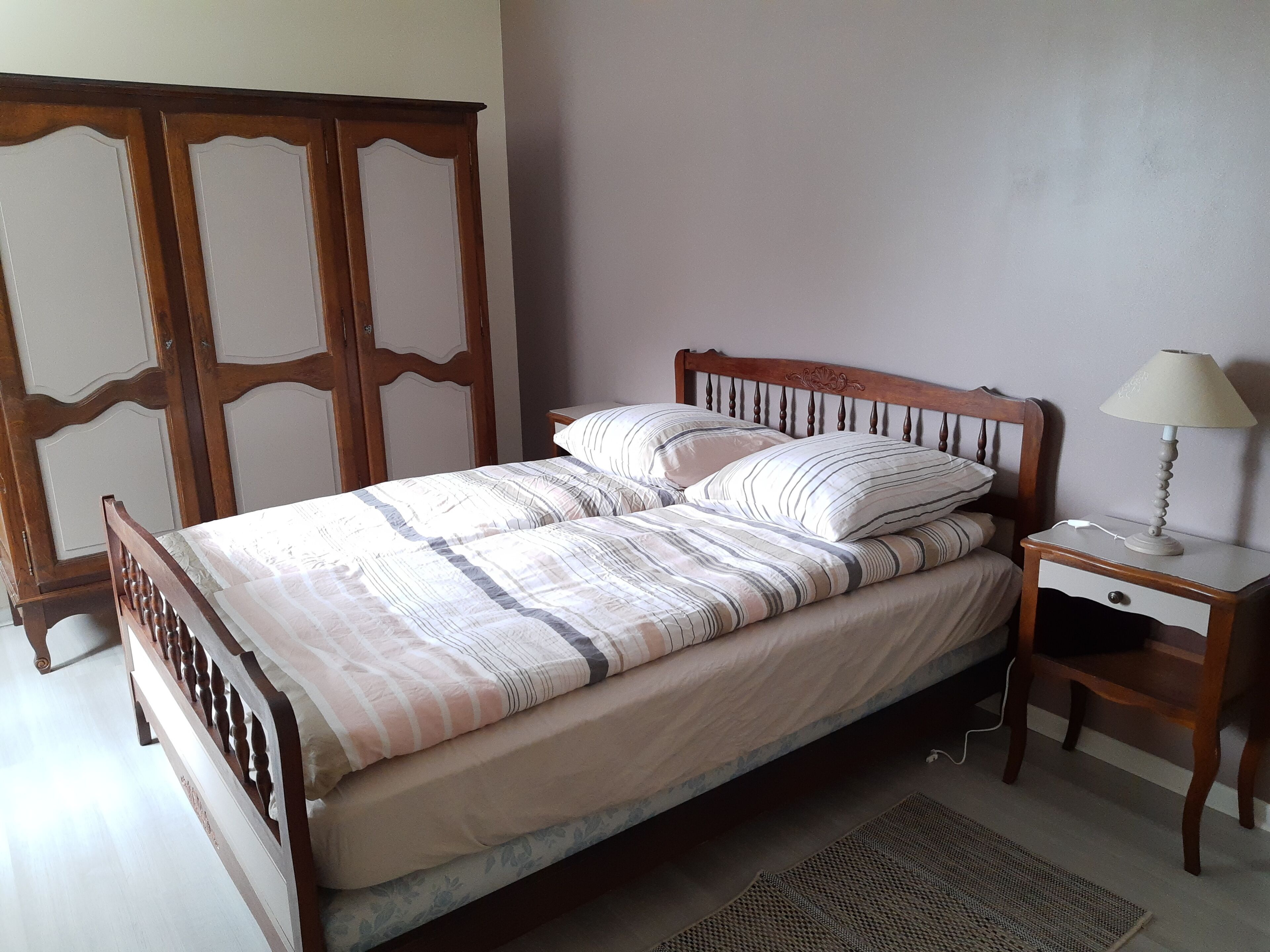 Una cama bien hecha con ropa de cama a rayas, un cabecero de madera, una mesita de noche con una lámpara y un tapete tejido en el suelo.