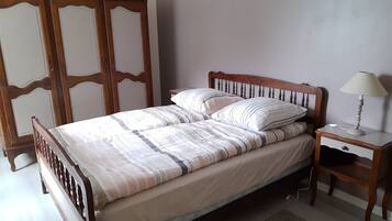 Una cama bien hecha con ropa de cama a rayas, un cabecero de madera, una mesita de noche con una lámpara y un tapete tejido en el suelo.