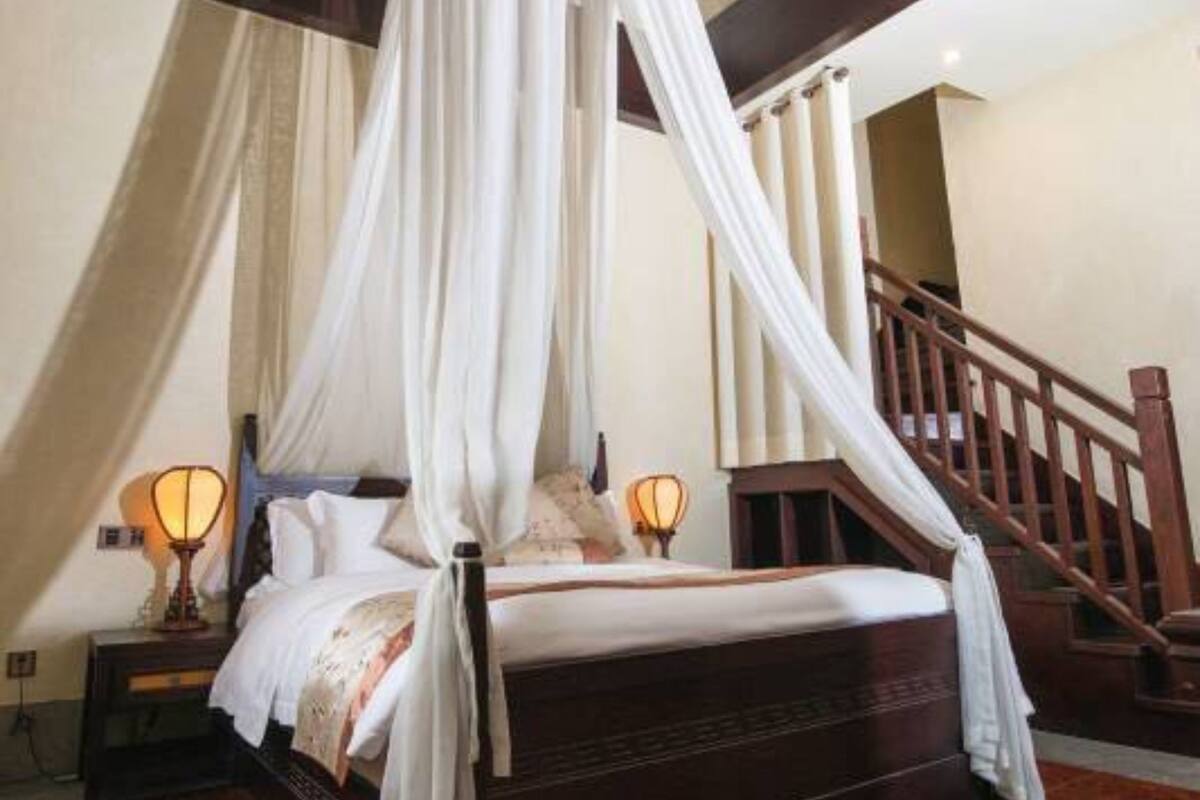 Ein Bett mit Himmelbett, hölzernes Kopfteil, ein Nachttisch mit Lampe und eine Treppe im Hintergrund.
