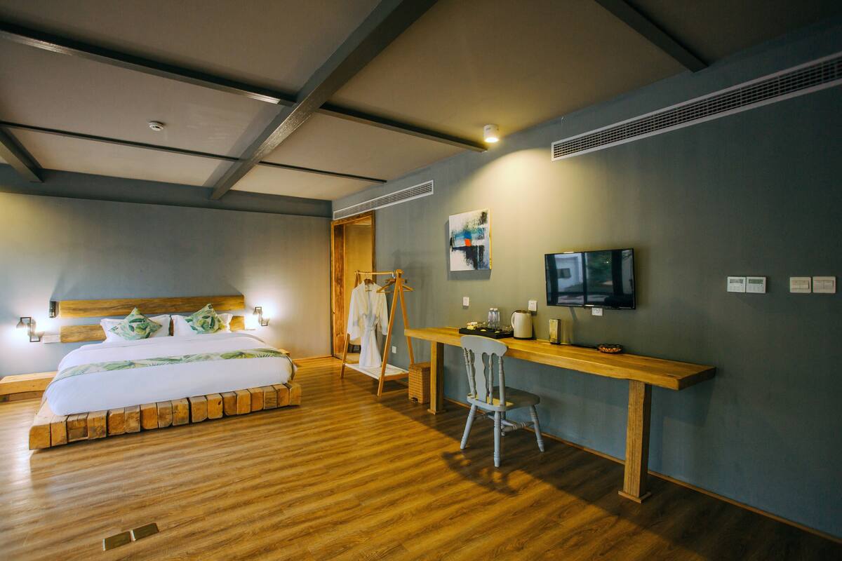 A hotel room with a wooden bed, a desk with a chair, a television, and artwork on the wall.