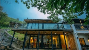 A two-story building with a covered outdoor seating area, stone steps leading up to the entrance, and a view of the surrounding greenery. - Floral Hotel Moganshan Cuiyu Resort (Huzhou)