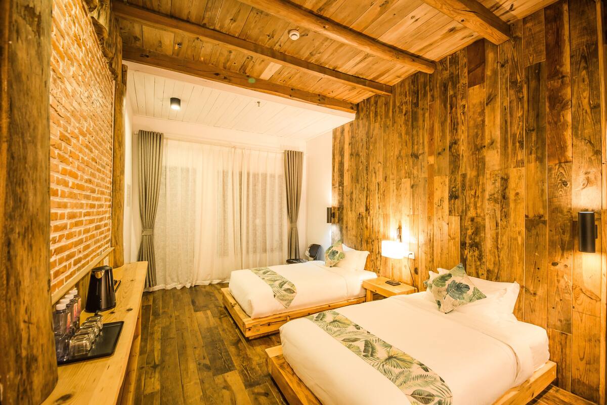 A room with two wooden beds, a brick wall, and a wooden ceiling.