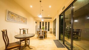 A dining area with a round table and chairs, a painting on the wall, and a glass door leading to another room. - Floral Hotel Moganshan Cuiyu Resort (Huzhou)