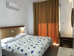 Une chambre d’hôtel comprenant un lit, une table de chevet, une chaise, un appareil de climatisation et une fenêtre avec des rideaux.