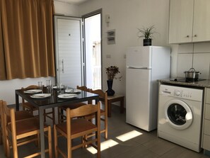 Une cuisine compacte comprenant une table à manger, des chaises, un réfrigérateur, un lave-linge et une plante en pot.