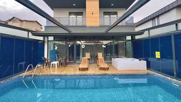 Ein moderner Poolbereich im Freien mit Liegestühlen und einem Whirlpool, umgeben von Glaswänden und einer Holzterrasse.