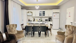 Ein modernes Wohnzimmer mit Essbereich, ausgestattet mit einer Couch, Sesseln, einem Couchtisch und einer Küche im Hintergrund.