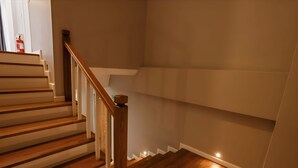 Eine Treppe mit Holzboden und Holzwandhandlauf, die zu einem Zwischenpodest mit weißer Wand und einer kleinen Leuchte führt.