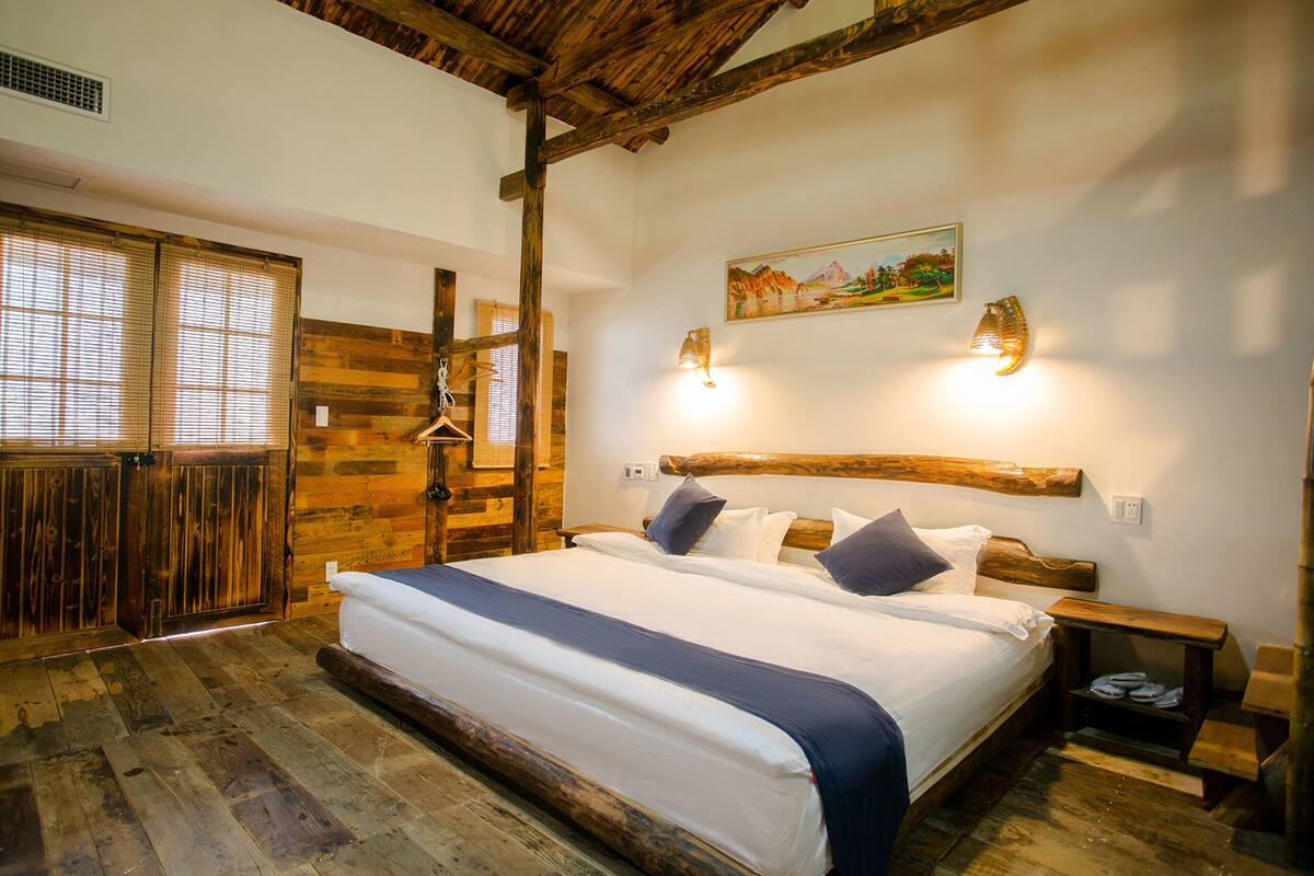 Ein Schlafzimmer mit Holzboden, einem großen Bett mit Kissen, einem Holz-Kopfteil und zwei Wandleuchten.