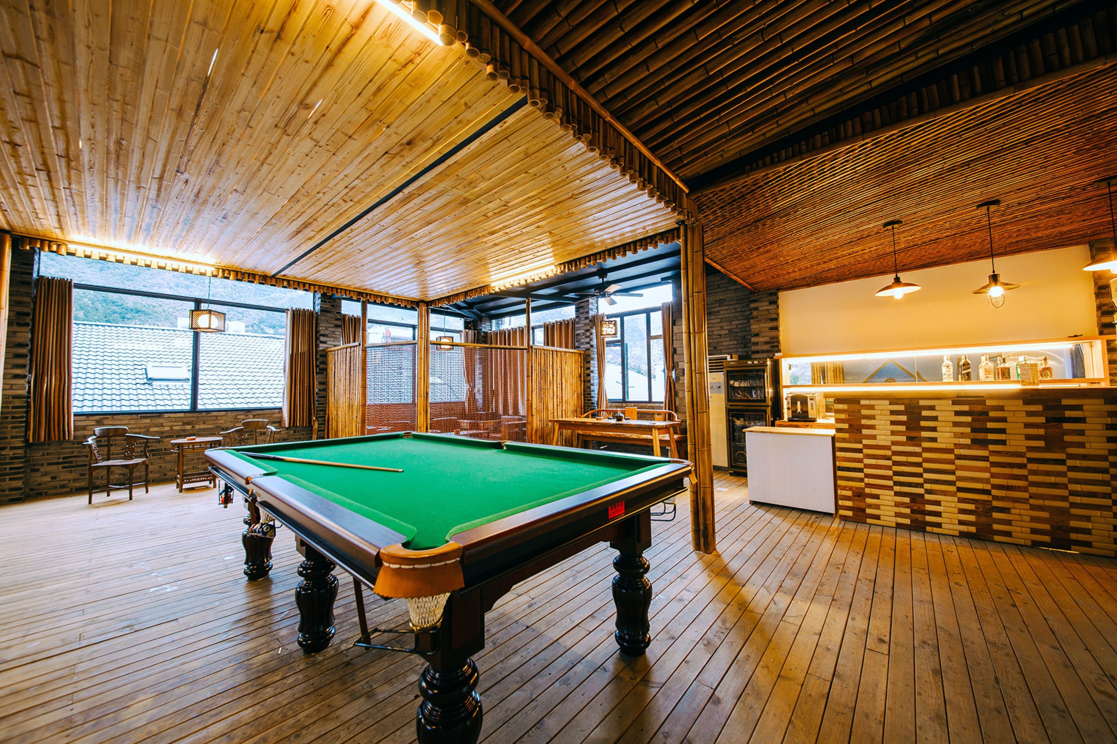 Ein Billardtisch in einem Raum mit Holzboden und hoher Decke. Im Hintergrund befinden sich Stühle und ein Tisch.