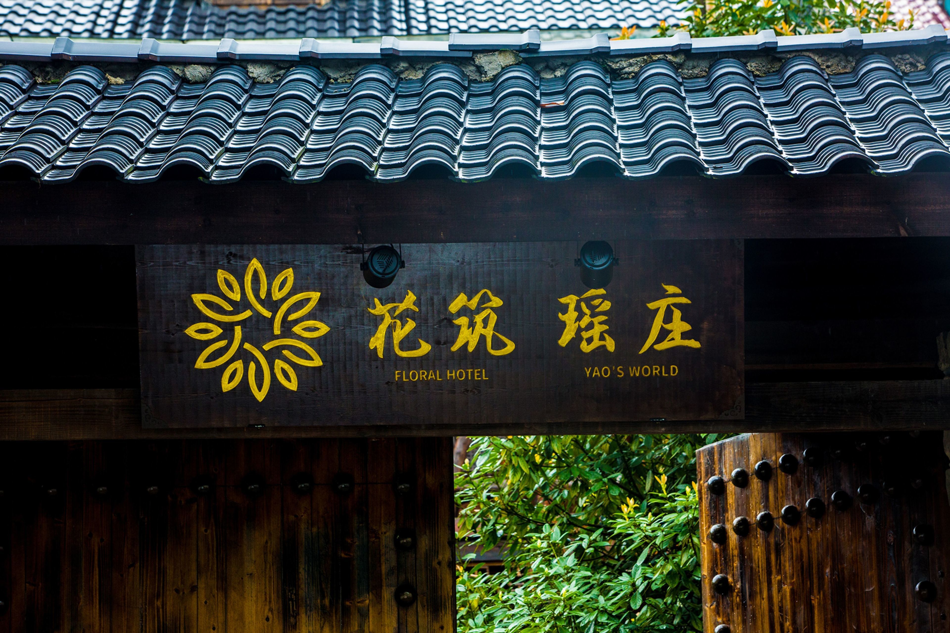 Un letrero de madera con texto amarillo y un logotipo floral, que indica un hotel llamado 'Yao's World'.