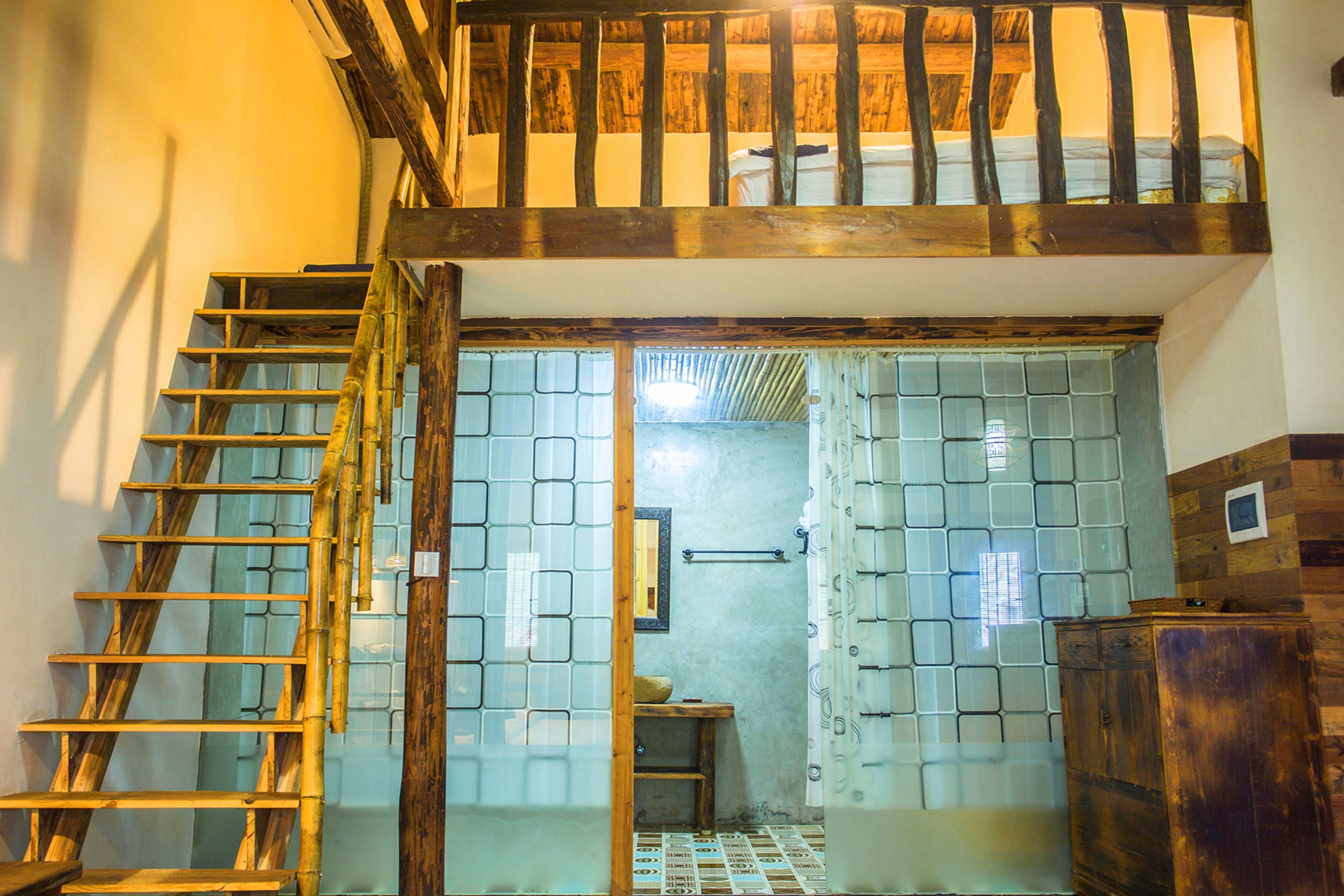 Een trap die leidt naar een slaapkamer op een entresol, met een houten plafond en uitzicht op het buiten.